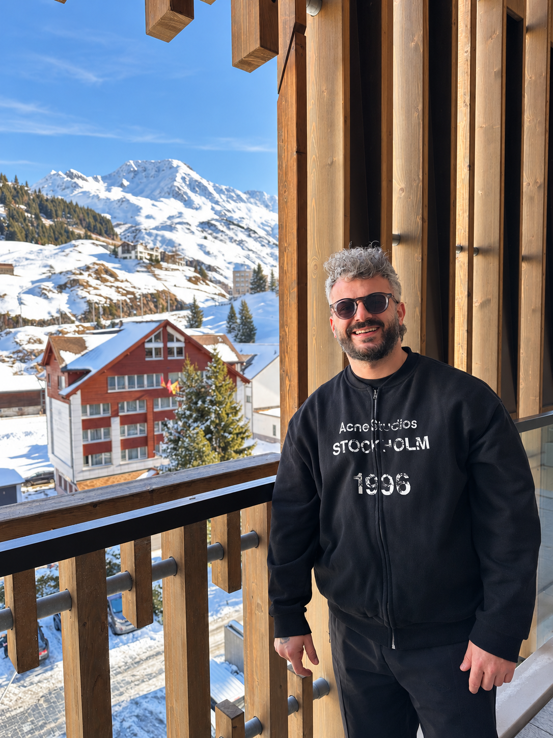 Gökhan Çokova standing on a balcony with snow-covered mountains behind him